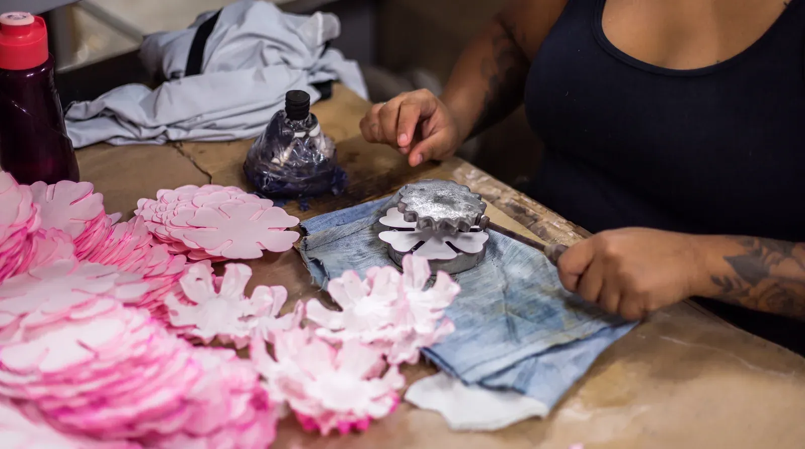 Artesã moldando uma forminha rosa sobre a fôrma metálica, com as peças cortadas ao lado