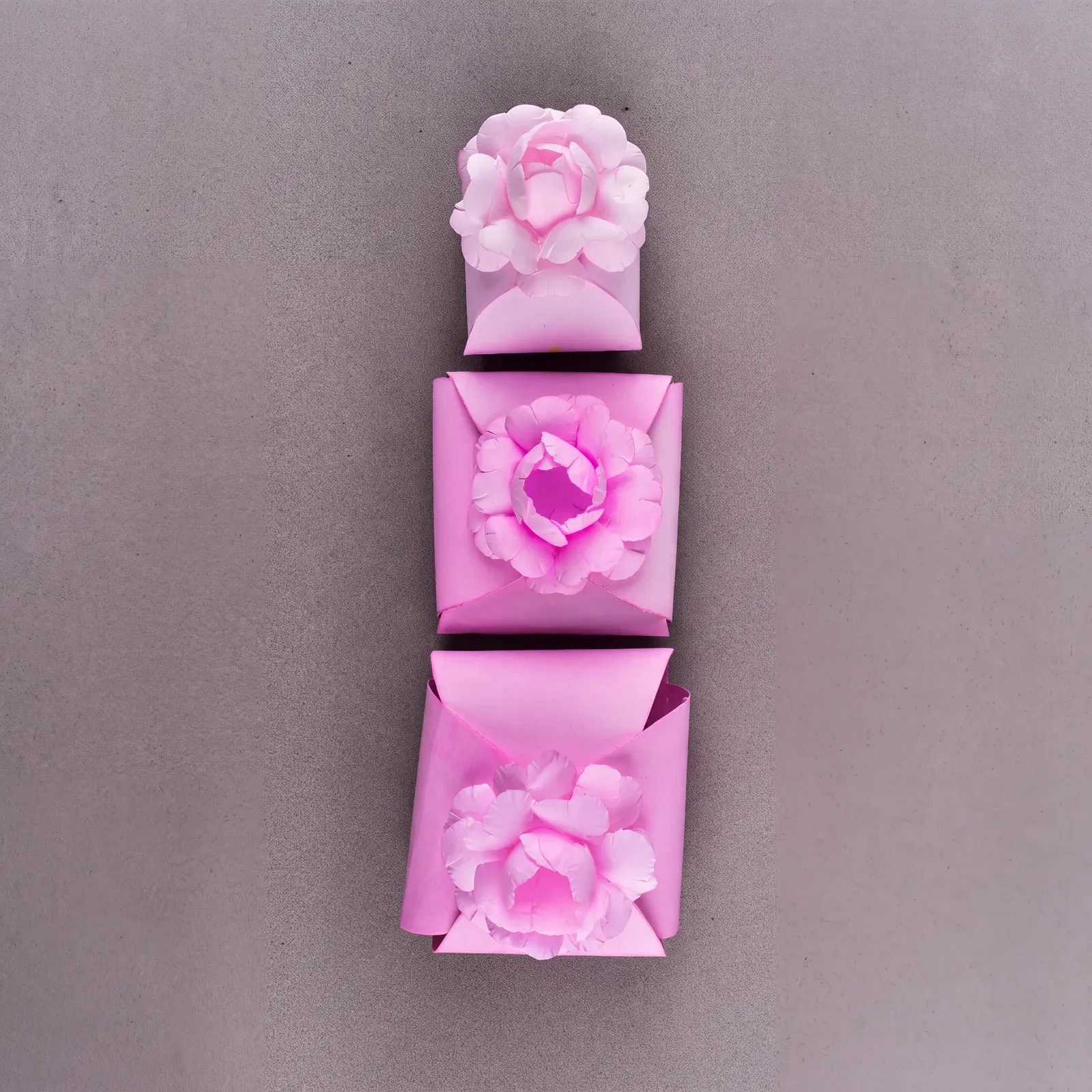 Três caixinhas cartonadas rosa da Embalarte com flor de papel no topo, em tamanhos diferentes